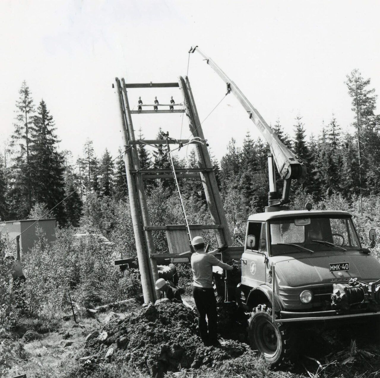 Miehet pystyttämässä sähköpylvästä Unimog apuna